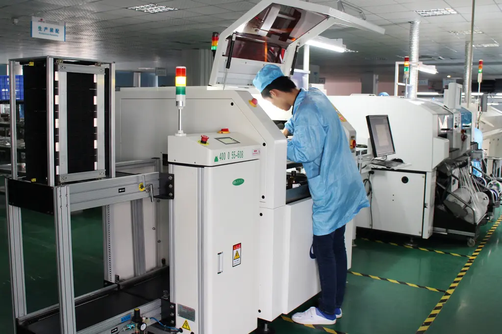 An electronics manufacturing technician working beside an SMT line of automated PCB production machines.